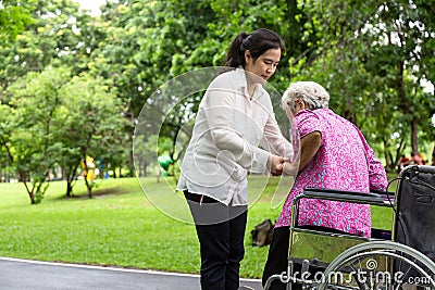 Female caregiver asian or young nurse support,helping senior woman to stand up from wheelchair in outdoor park,patient mother with Stock Photo