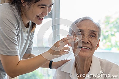 Female caregiver assisting to apply sunscreen lotion on the face of senior woman,granddaughter using skin care cream for elderly Stock Photo