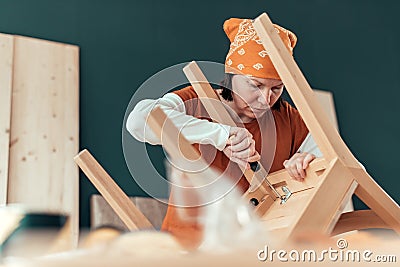 Female carpenter repairing wooden chair seat in workshop Stock Photo