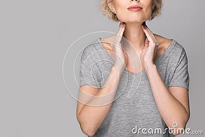 Female checking thyroid gland by herself. Close up of woman in white t- shirt touching neck with red spot. Thyroid Stock Photo