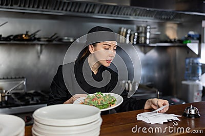 Female chef checks the prepared dish with the paid check in kitchen of the restaurant Stock Photo