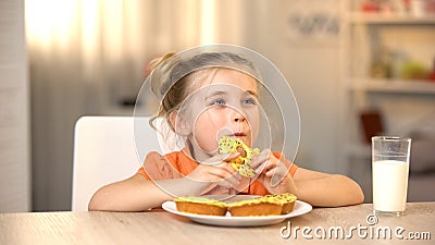 Female child eating tasty donut, milk glass on table, sweet snack, nutrition Stock Photo