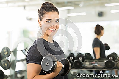 Female Client Smiling While Doing Dumbbell Exercise In Gym Stock Photo