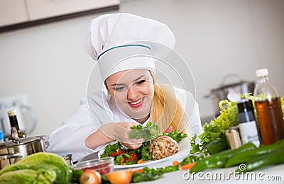 Female cook arranging herbs decoration on plate with salad Stock Photo