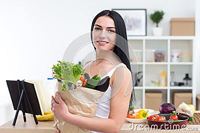 Female cook holding bag full of greens, just came back from market, ready to prepare healthy food with cookbook recipe Stock Photo