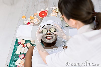 Female cosmetologist in uniform and protective gloves doing cucumber mask on eyes for relaxation in beauty salon Stock Photo