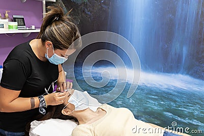 Female customer with a medical face mask getting her eyebrows fixed - Covid-19 protection concept Stock Photo