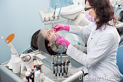 Female dentist with dental tools - mirror and probe treating patient teeth at dental clinic office. Medicine, dentistry Stock Photo