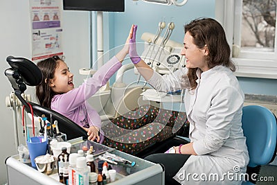 Female dentist and girl patient satisfied after treating teeth at dental clinic office, smiling and doing high-five Stock Photo