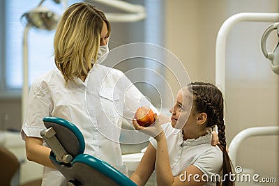 Female dentist gives apple for smiling teenage girl in modern clinic Stock Photo