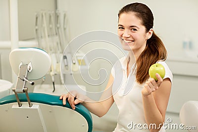 Female dentist smiling and holding a green apple, dental care and prevention concept Stock Photo