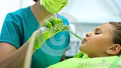 Female dentist using saliva ejector, teenage girl sitting in chair frowning Stock Photo