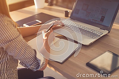 Female designer using laptop, sketching at blank notepad. Woman hand writing in notebook on wooden desk. Stock Photo