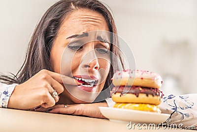 Female desperately trying to resist donuts, biting her finger Stock Photo