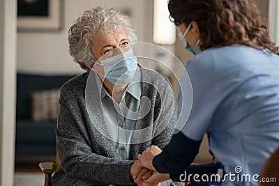 Female doctor consoling senior woman wearing face mask during home visit Stock Photo