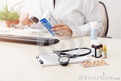Female doctor entering medication information into computer, there are various drugs on table Stock Photo