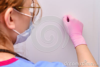A female doctor in a medical mask knocks on the door of a patient with a coronavirus. Close-up of a nurse in protective gloves Stock Photo