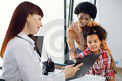 Female doctor pediatrician showing medical report or medical test results to young African mother and her tenn daughter Stock Photo