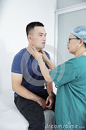 Doctor palpating neck of man Stock Photo