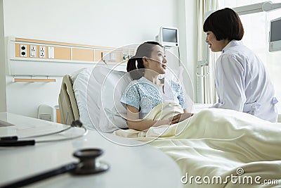 Female doctor sitting on hospital bed and discussing with young female patient Stock Photo