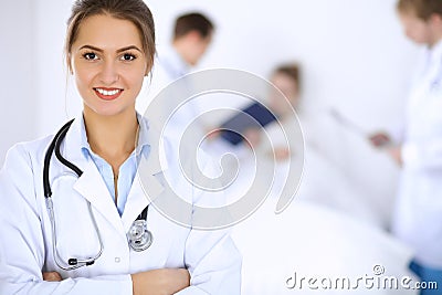 Female doctor smiling on the background with patient in the bed and two doctors Stock Photo