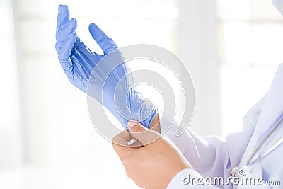 Female doctor with a stethoscope on one shoulder putting on sterile gloves Stock Photo