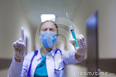 Female doctor with syringe in hand. Showing attention sign. She going to make injection, virus treatment. Focus on the Stock Photo