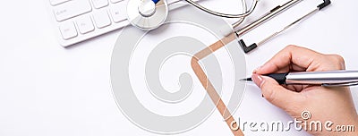 Female doctor writing a medical record case over clipboard on white working table with stethoscope, computer keyboard. Top view, Stock Photo