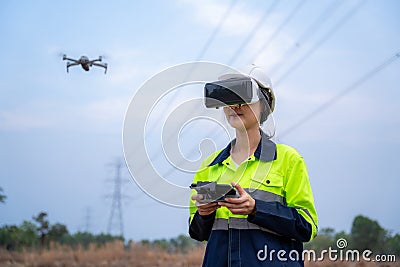 A female electrical engineer wearing vr goggles flying drone to explore aerial view equipment on high voltage pylons at power Stock Photo