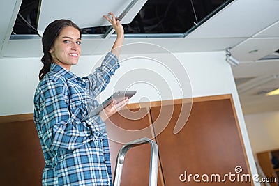 Female electrician standing on ladder and holding tablet Stock Photo