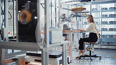 Female Electronics Engineer Works with Robot, Manipulating it with Hand and Checking Data on Laptop Stock Photo