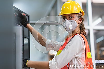 Female Engineer wear face mask with safety vest and yellow helmet operating control CNC Machinery at factory Stock Photo