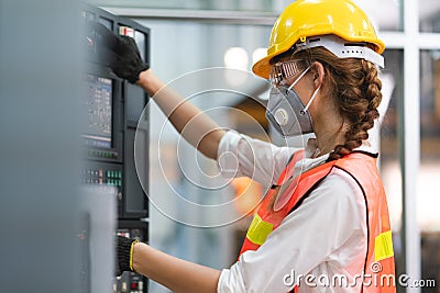 Female Engineer wear face mask with safety vest and yellow helmet operating control CNC Machinery at factory Stock Photo