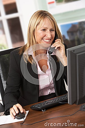 Female Estate Agent Talking On Phone At Desk Stock Photo