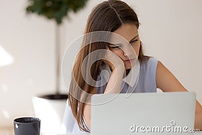 Female feels boredom seated at desk looking at laptop screen Stock Photo