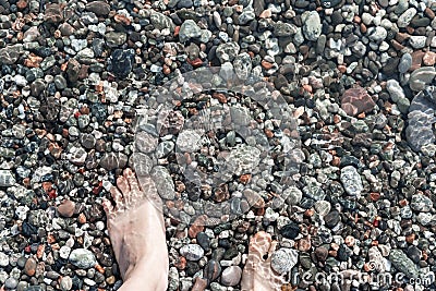 Female feet in sea water on a pebble shore top view in summer, many pebbles, copy space, relaxation in nature, swimming in sea Stock Photo