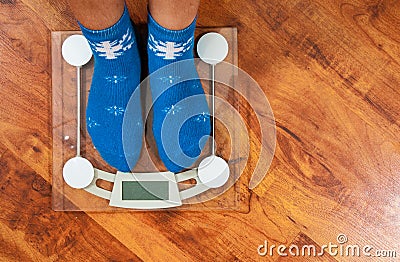 Female feet standing on electronic scales for weight control in Christmas socks on wooden floor background. with copy space. Stock Photo