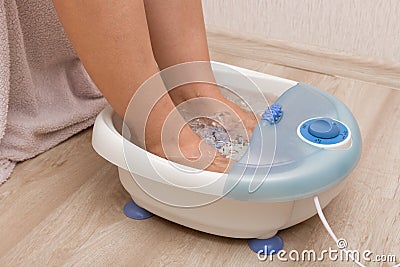 Female feet in a vibrating foot massager. Electric massage foot bath. Pedicure and foot care. Stock Photo