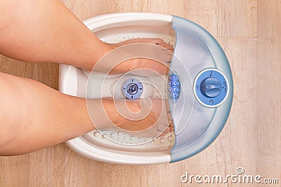 Female feet in a vibrating foot massager. Electric massage foot bath. Pedicure and foot care. Stock Photo