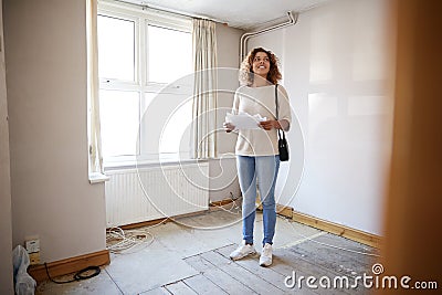 Female First Time Buyer Looking At House Survey In Room To Be Renovated Stock Photo