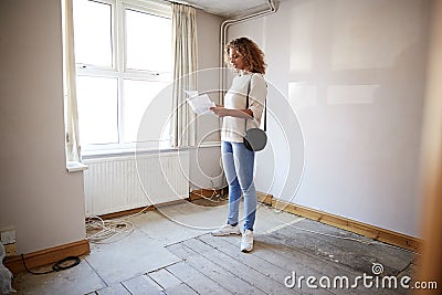 Female First Time Buyer Looking At House Survey In Room To Be Renovated Stock Photo