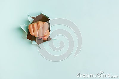 Female fist punching through blue paper background. War, struggle, conflict, feminist concept. Banner with copy space Stock Photo