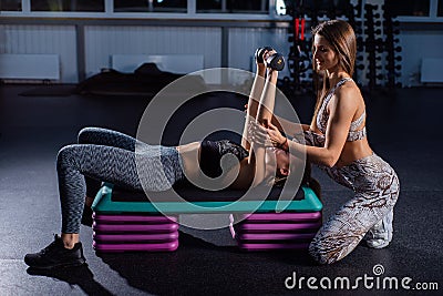 Female fitness instructor conducts personal training. Young attractive woman doing bench press lying on the platform Stock Photo