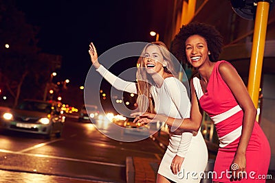 Female friends hailing taxi on city street at night Stock Photo