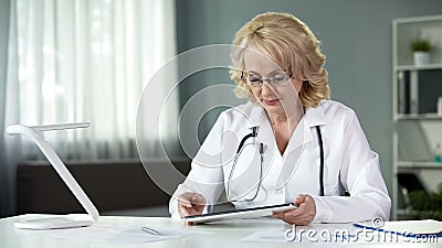 Female general practitioner reading patient's online medical records on tablet Stock Photo