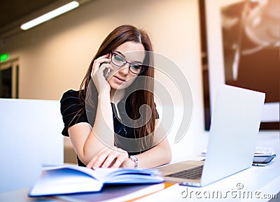 Female in glasses skilled advertiser reading information from textbook during mobile phone conversation Stock Photo