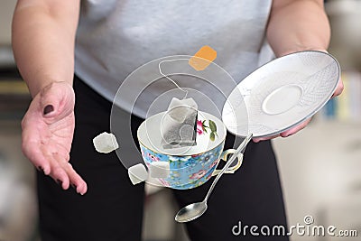 A female in gray t-shirt dropping teacup with teabag sugar cubes and spoon Stock Photo