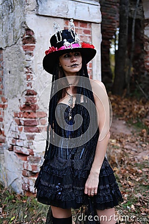 Female Halloween look. A woman in a black dress with a corset, a top hat decorated with skeleton figures poses for the Stock Photo