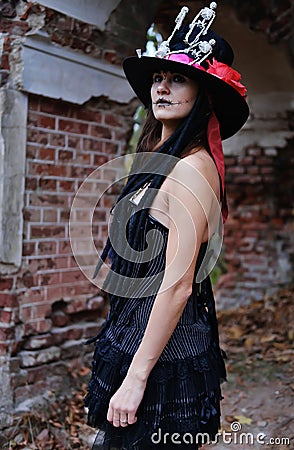 Female Halloween look. A woman in a black dress with a corset, a top hat decorated with skeleton figures poses for the Stock Photo