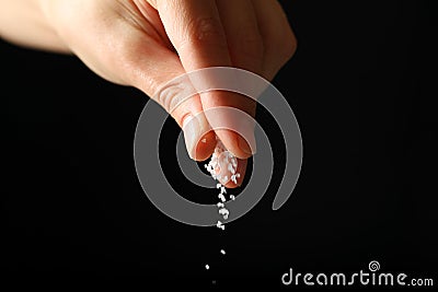 Female hand adding salt on black background Stock Photo